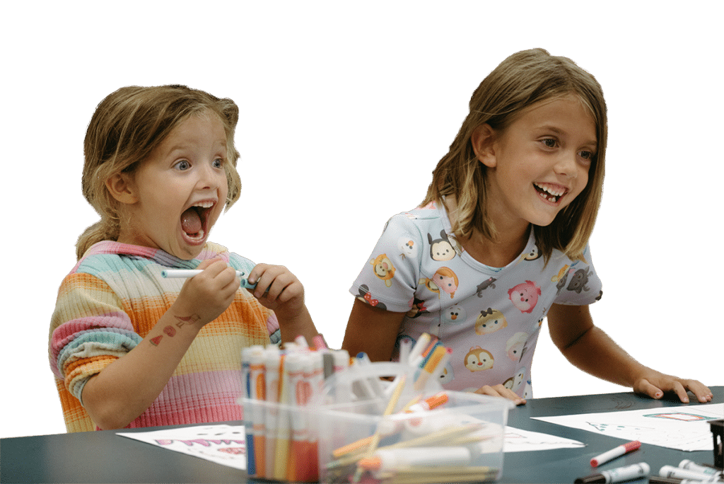 Two kids at a table in the classroom as they color with crayola markers and colored pencils