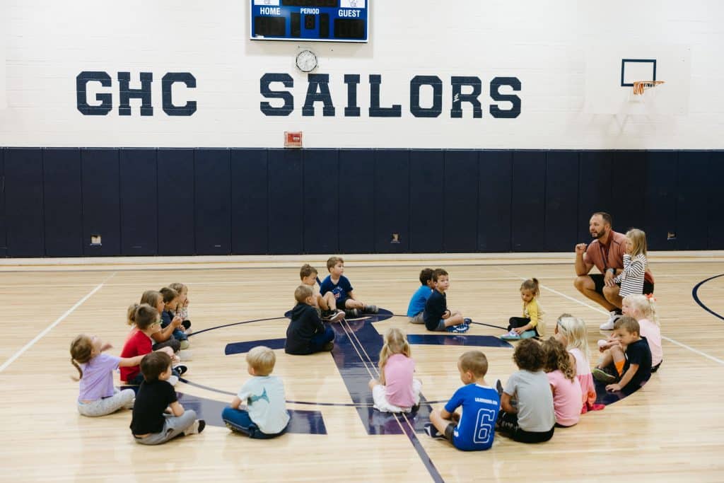 Younger students in the gym getting ready for instruction from teacher as they all sit in a circle