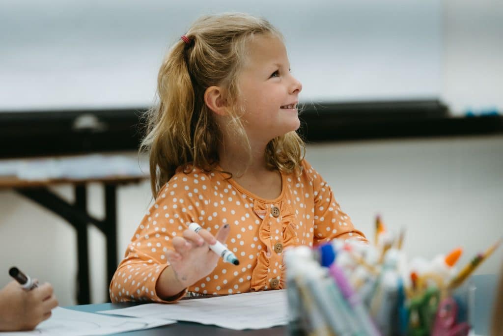 Kids at a table in the classroom as they color with crayola markers