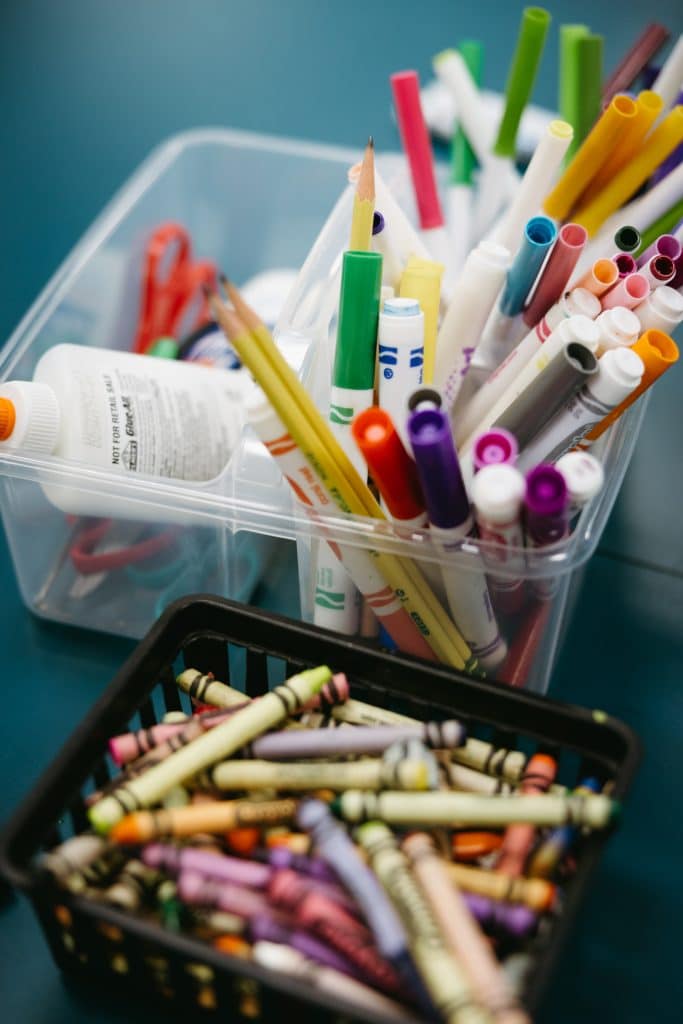 Close up of markers in container with scissors and pencils and a bucket with crayons